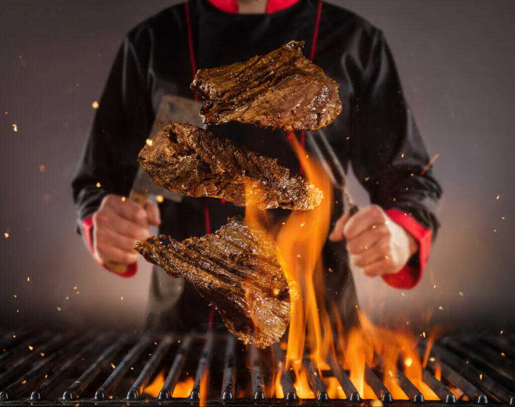 chef flipping steaks on a fiery grill