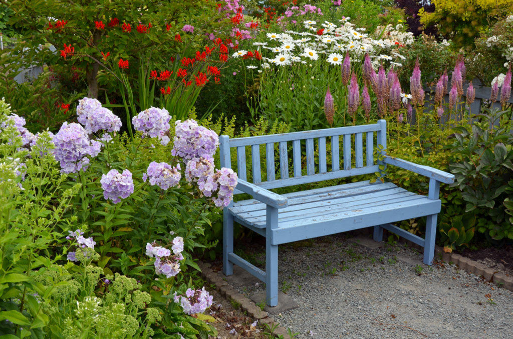 Cozy bench surrounded by flowers makes a great place to relax in the yard.